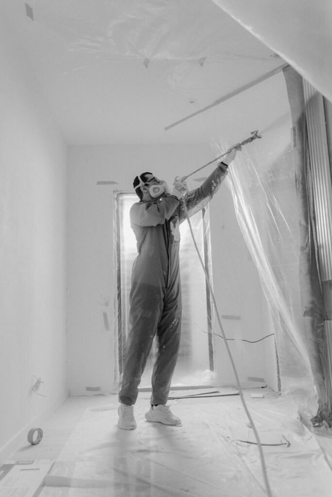 A worker in a respirator uses a spray gun on a construction site during renovation.